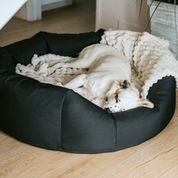 Round Dog Bed with a dog sleeping on a cream color blanket