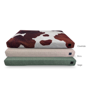 Stack of three dog beds displaying cowhide, sage green, and ecru tan color bed covers