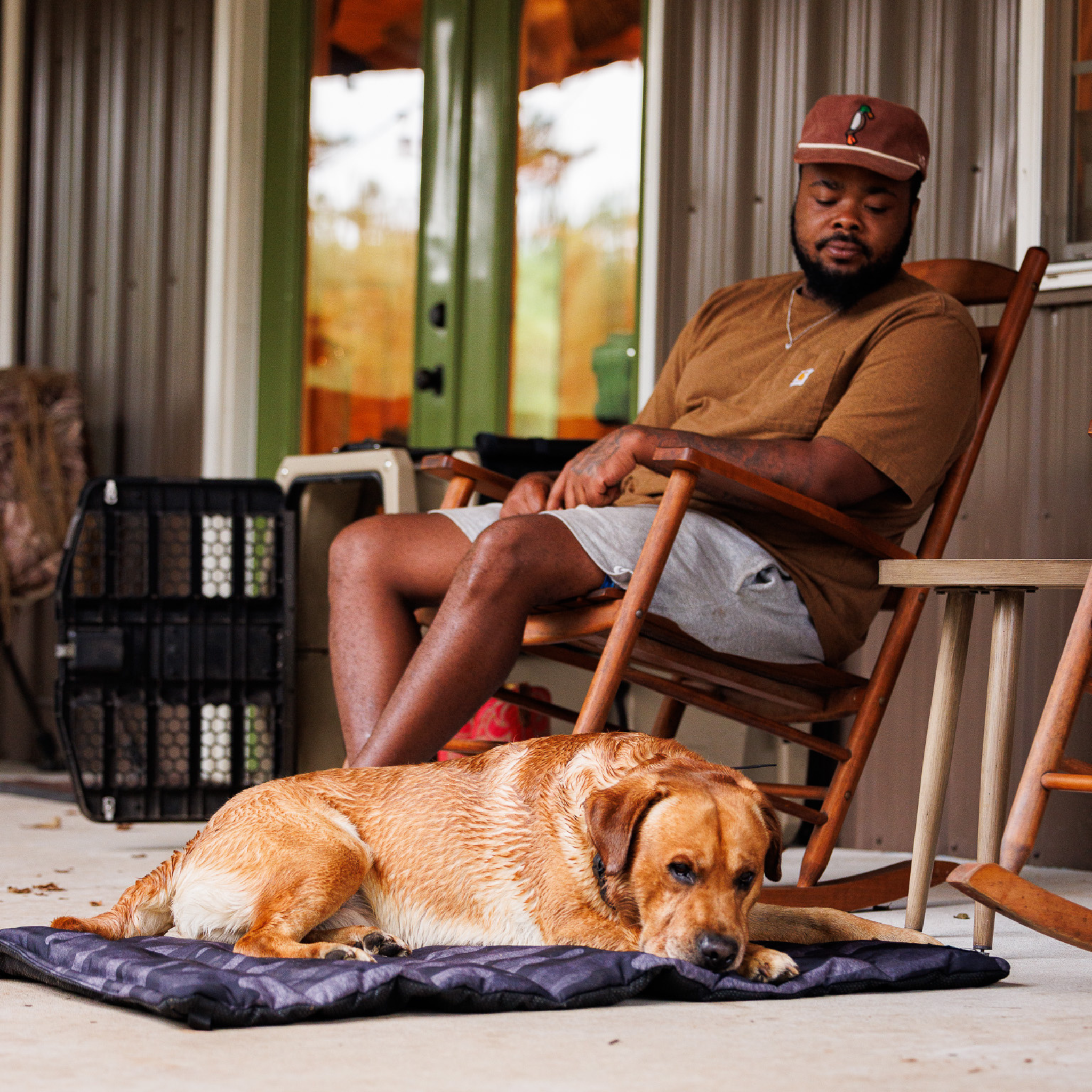 Man sitting on a chair with a dog on a trailblazer mat on a porch